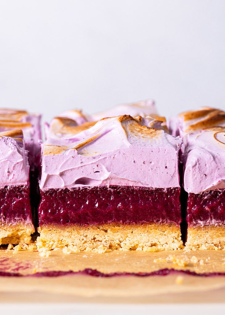 Blueberry meringue bars, sliced into individual portions, on a sheet of brown parchment paper.