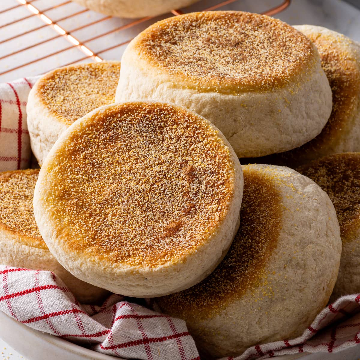 Gluten free English muffins piled on top of a checkered napkin.