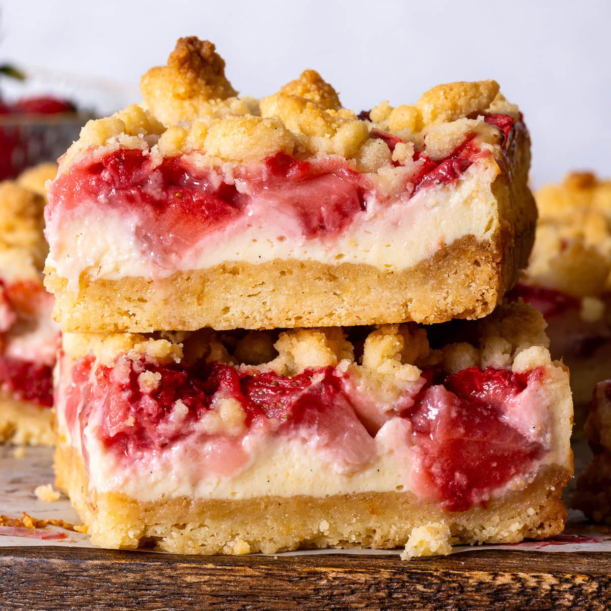 A stack of two strawberry cheesecake bars on top of a wooden serving board.