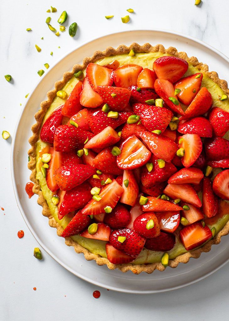 Overhead view of a pistachio tart, decorated with fresh strawberries and chopped pistachios.