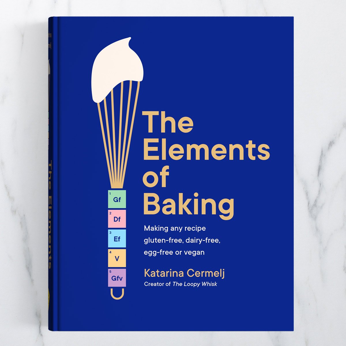 The Elements of Baking cookbook on a white marble background.